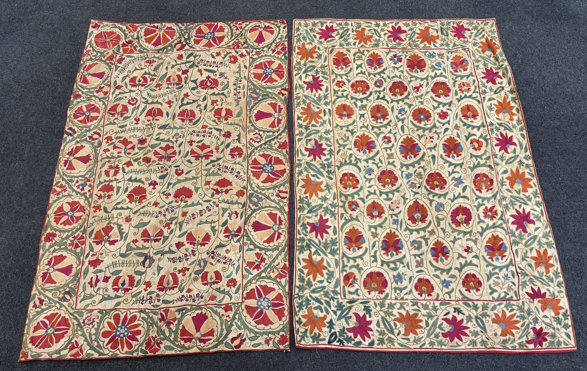 Two Uzbekistan Suzani, late 19th / early 20th century, embroidered hangings, on thick cotton, converted later to curtains, both richly embroidered with a wide floral frieze and a central all over floral design using Bukh